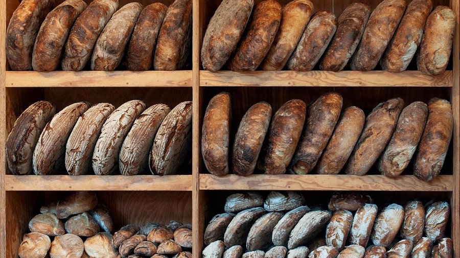 In einem braunen Regal mit sechs Fächern sind verschiedene Brote und Brötchen aneinandergelehnt.