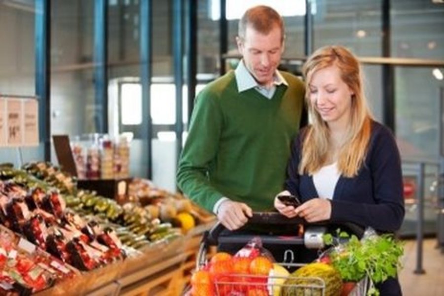 Junges Paar mit Einkaufswagen und Handy in der Hand im Supermarkt vor dem Gemüsestand mit dem Handy in der hand 