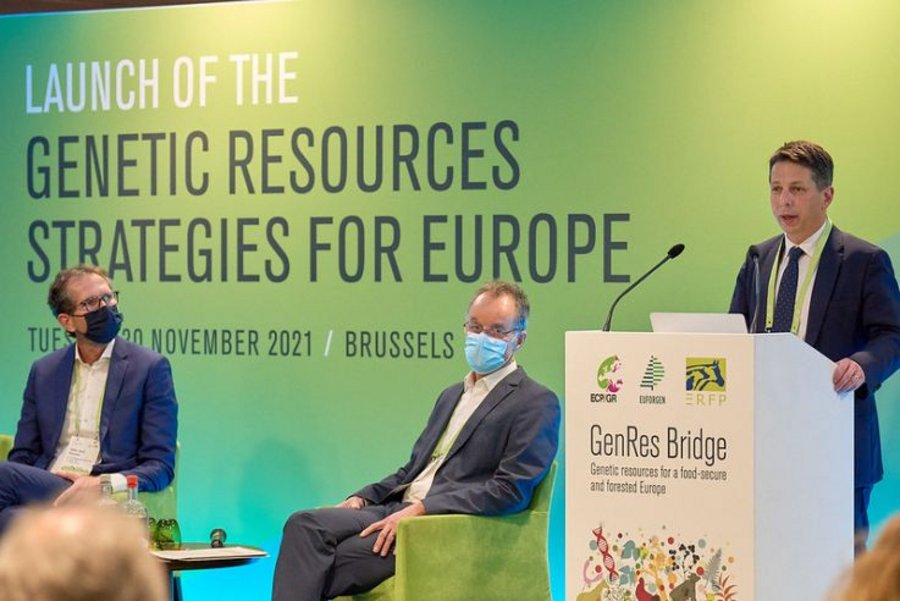 Panel discussion with moderator and two male panelists. The background shows a green project banner.