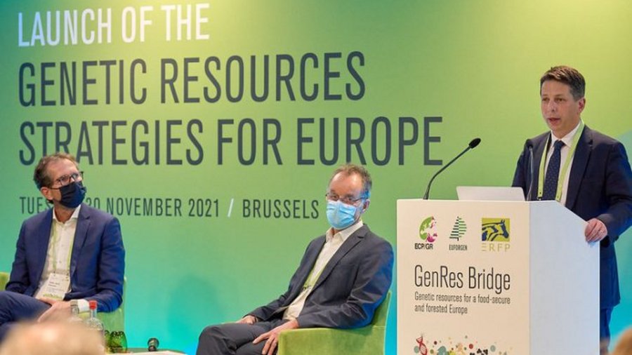 Panel discussion with moderator and two male panelists. The background shows a green project banner.