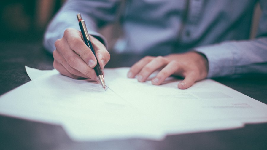 Man signing various documents in front of him on the table. Click leads to enlarged view